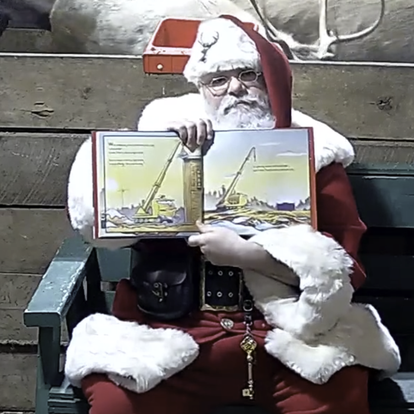 Man in red suit with white fur lining and matching hat holds book open in front of reindeer